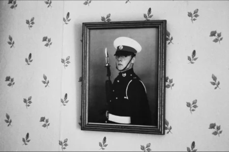 A portrait of the groom in uniform hangs on the wall of his family home. Framed portrait of the groom in Royal Marine uniform hanging on a wall.