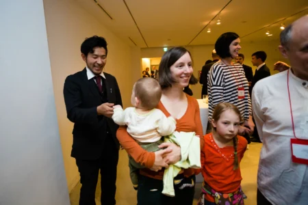 The maître d’ greets delegates arriving for a conference welcome reception, including a professor carrying a baby, during an academic event in Japan. Conference Welcome Reception in Osaka, Japan