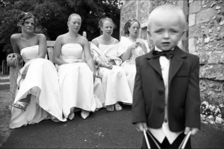 The page boy and bridesmaids wait outside the church before the service begins. Page boy and bridesmaids waiting on a bench outside the church before the wedding ceremony.