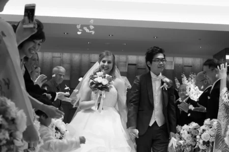 The bride and groom walk down the aisle as guests throw confetti. Bride and groom walking down the aisle as guests throw confetti after their wedding ceremony in Osaka, Kansai, Japan.