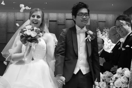 The couple celebrate with their guests during a joyful confetti walk. Bride and groom smiling as confetti is thrown after their wedding ceremony in Osaka, Japan.